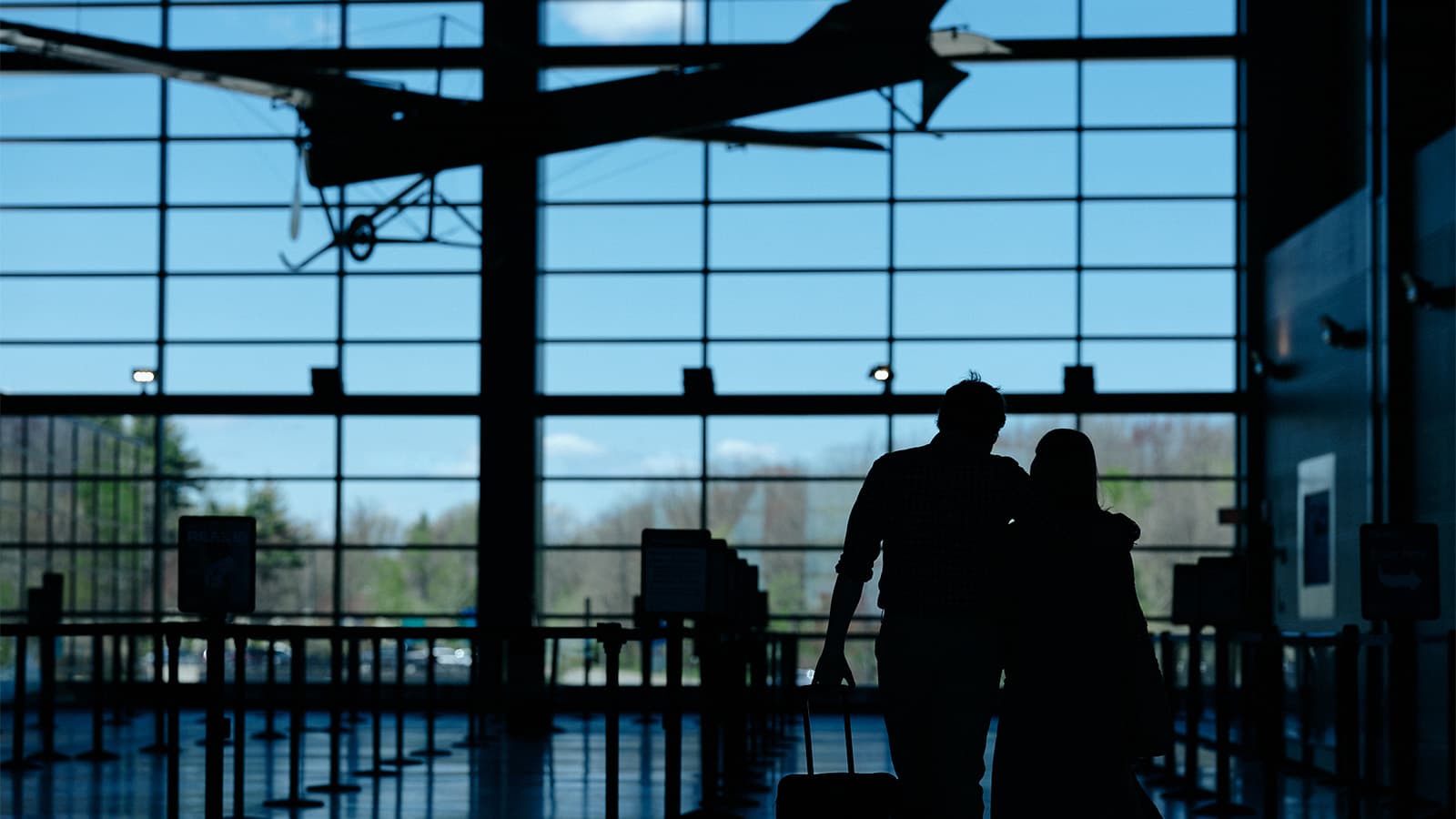A couple embraces in an airport terminal while looking out the window