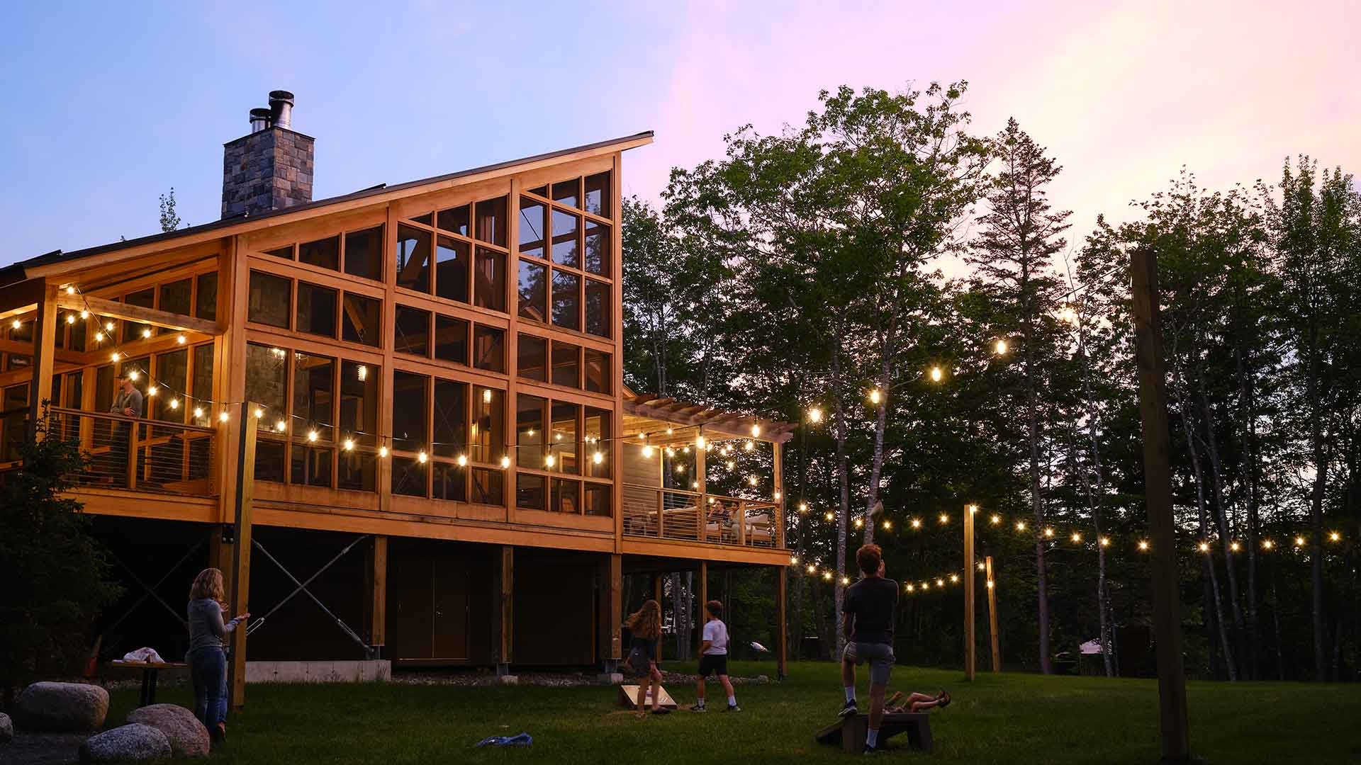 A modern cabin with large windows overlooking a grassy yard.