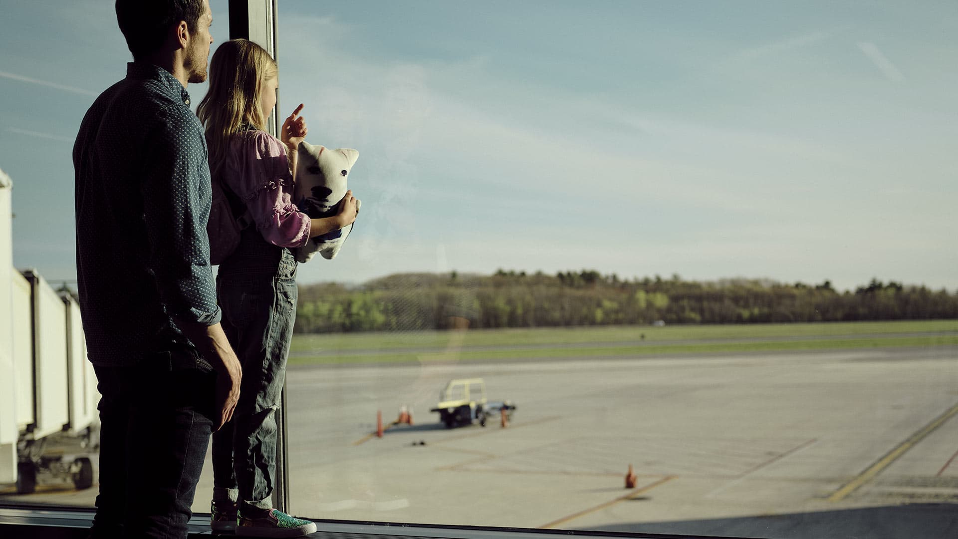 A man and child look out the airport window at the planes on the tarmac.