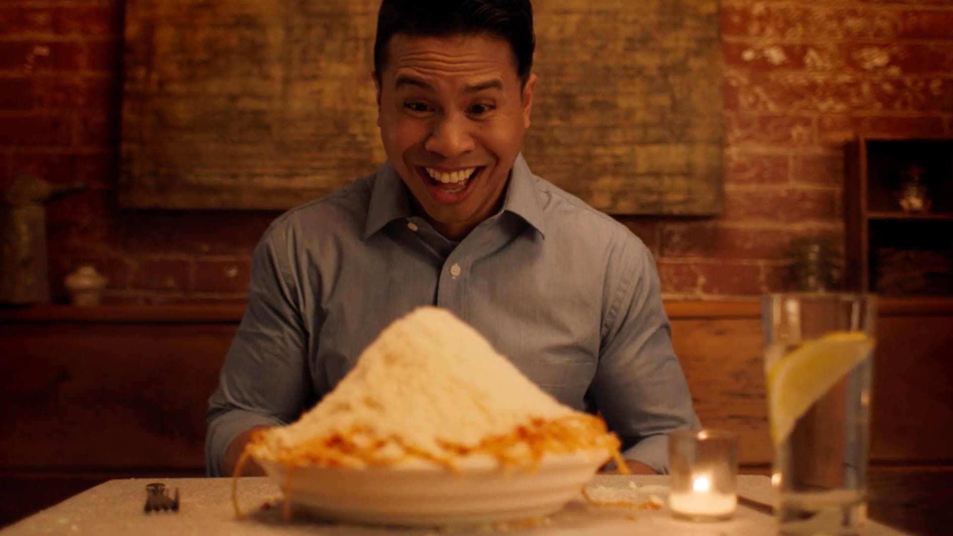 A man smiling in front of an oversized bowl of spaghetti.