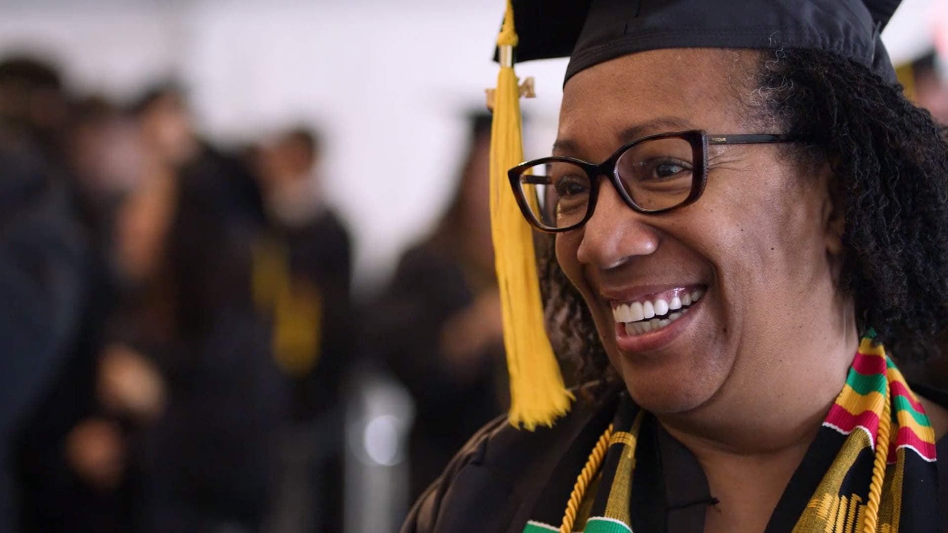 A woman in a graduate outfit smiles proudly on graduation day.