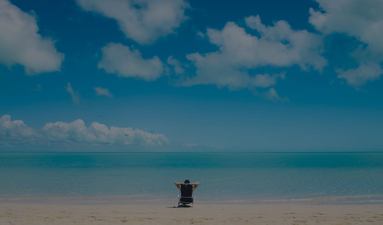 A lone person sits on a beach looking at the water