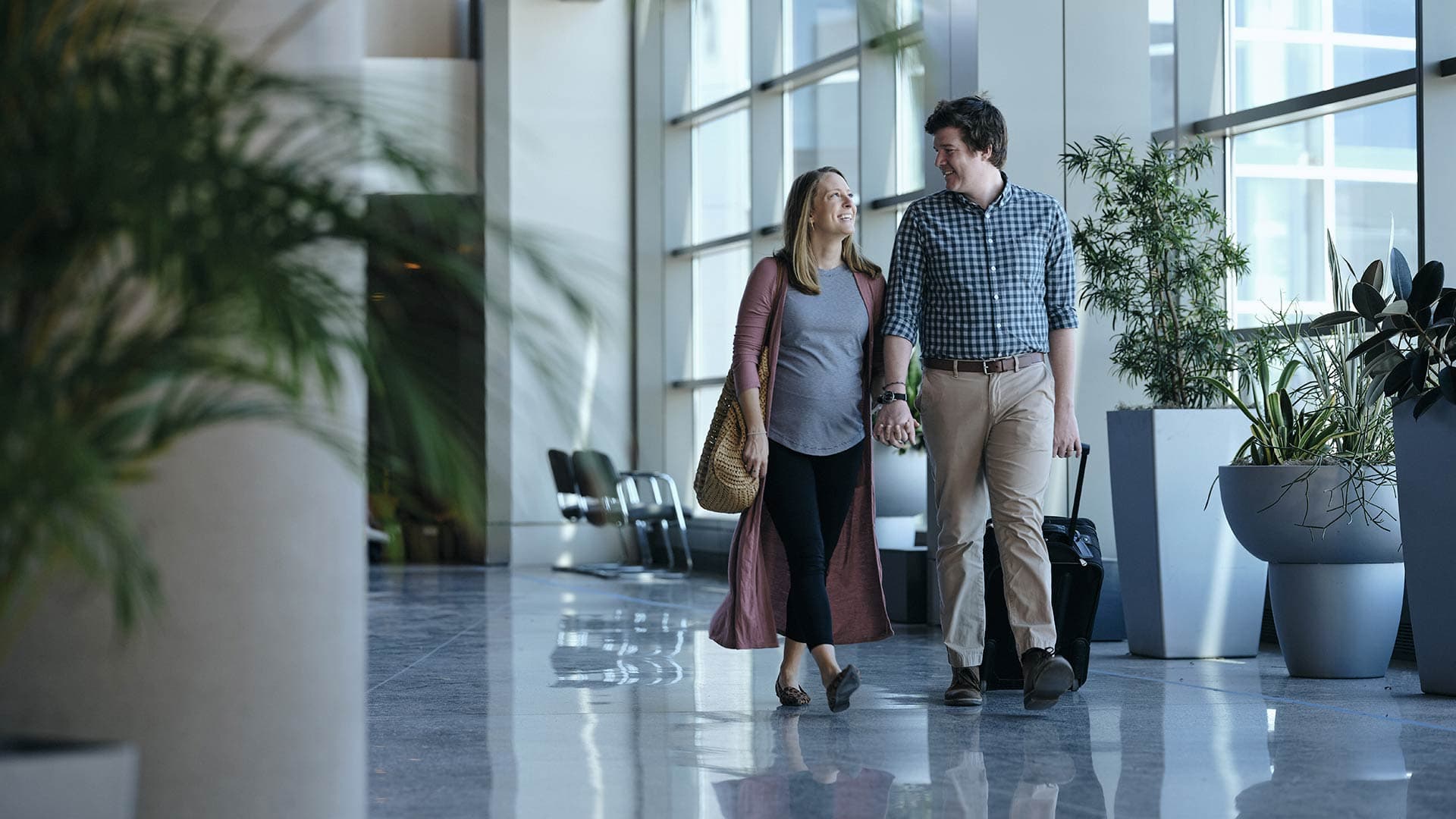 A couple walks happily through the airport carrying their luggage and smiling.